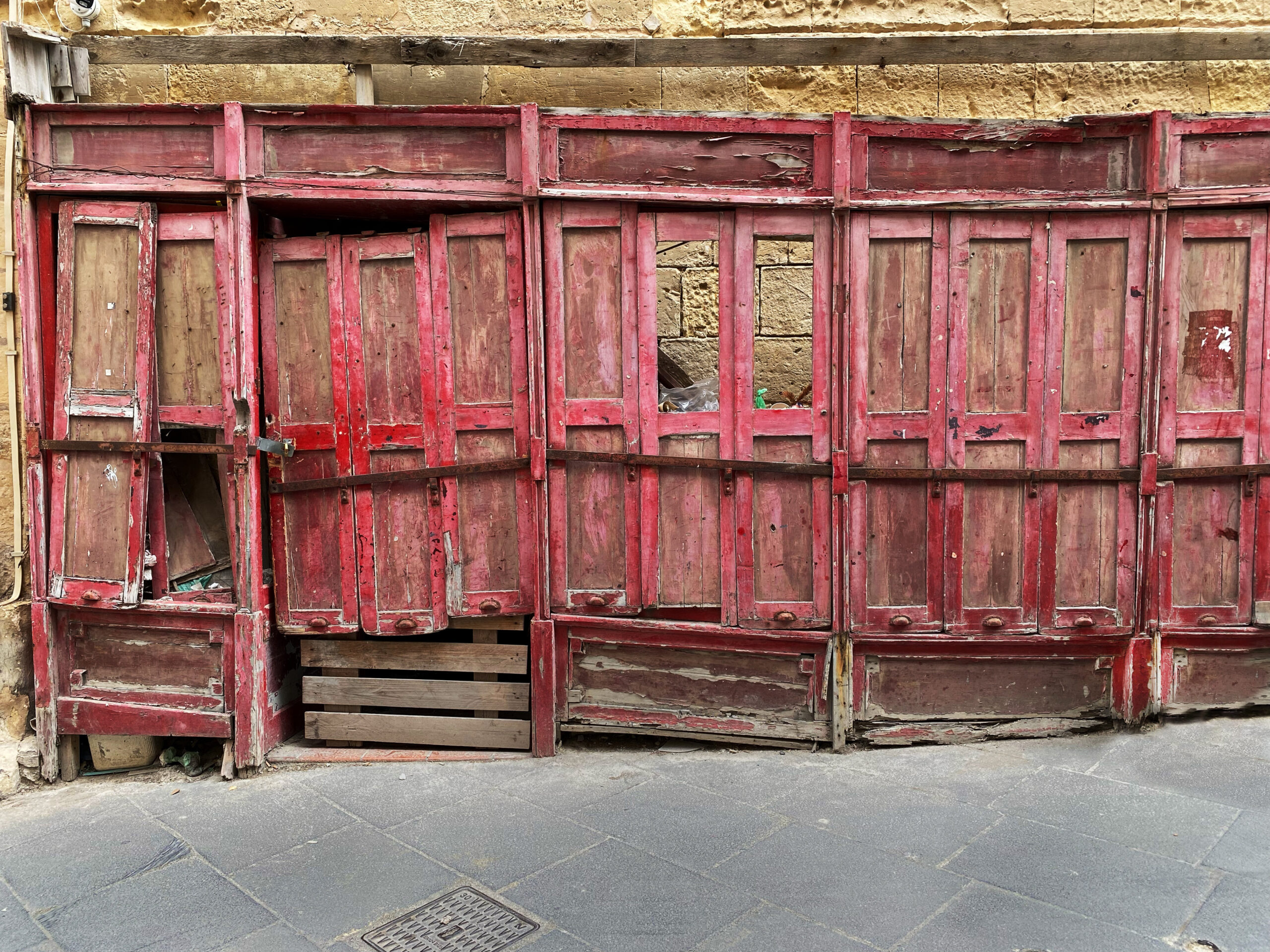 Porte in legno rosso con elementi mancanti e vernice scrostata nella città di Valletta, Malta, ph. Richard Bryant